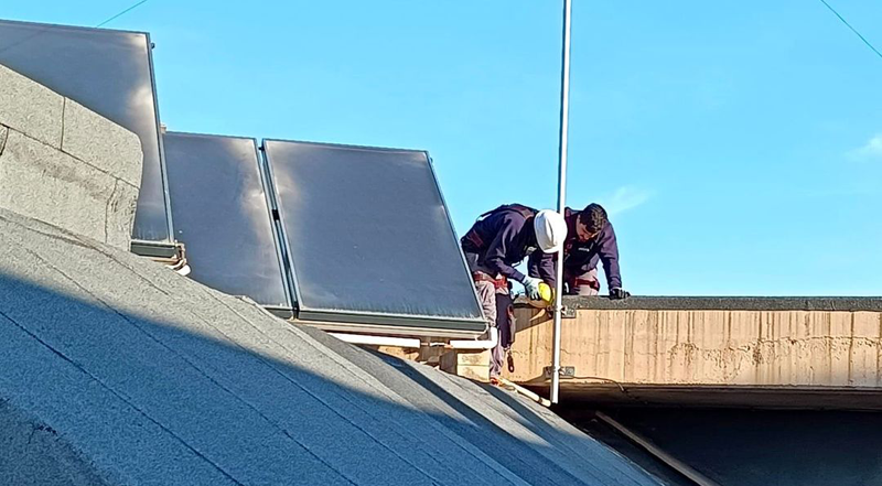Dos técnicos instalando placas solares en la cubierta de un edificio.