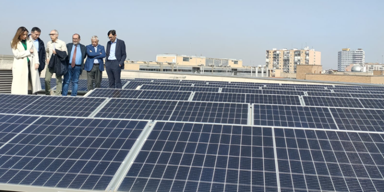 Placas solares instaladas en la cubierta de un edificio y varias personas visitando la instalación.