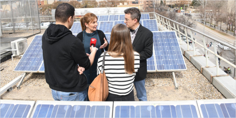 Cuatro personas en la azotea de un tejado en la que están instaladas placas solares.