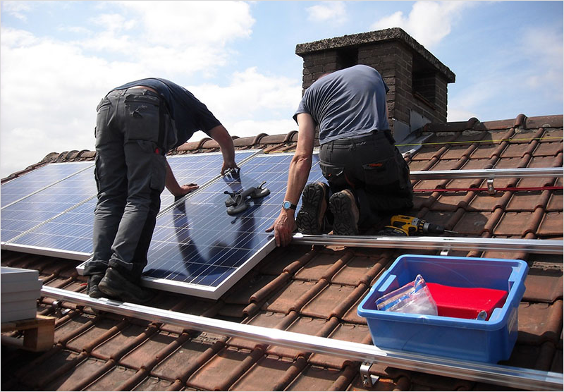 Dos instaladores de placas solares en un tejado colocando paneles solares.